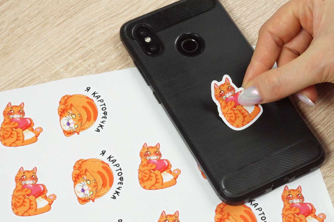 Показано приклеивание наклейки на смартфон.